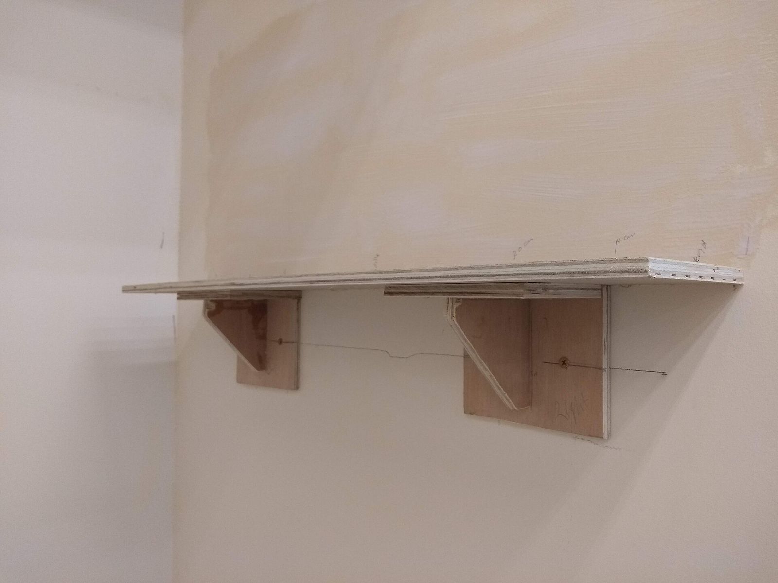A wooden shelf held to a wall by two wooden brackets.